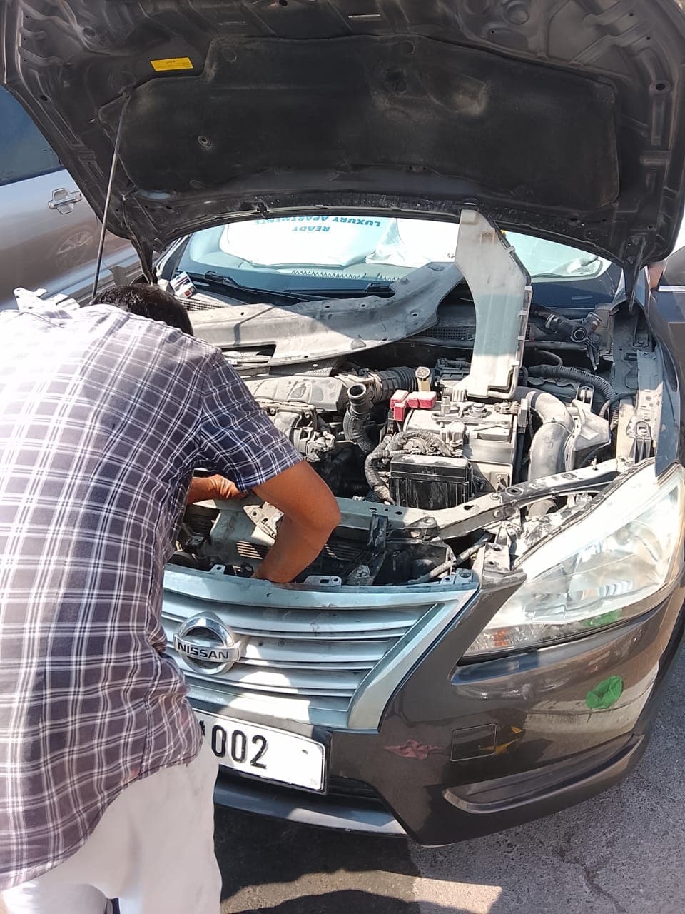 Technician working under the hood of a Nissan sedan
