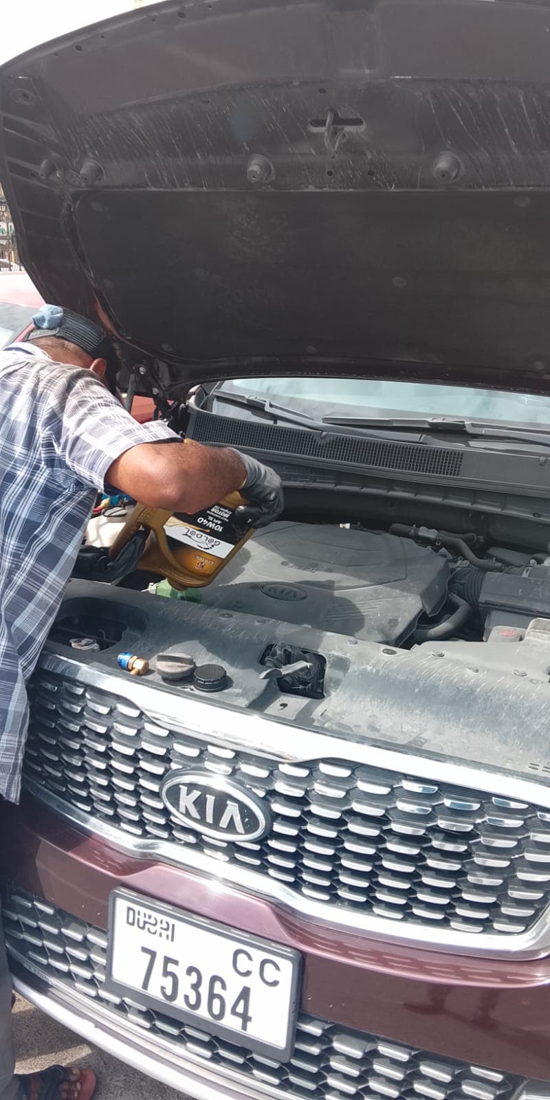 Technician topping up engine oil on a Kia
